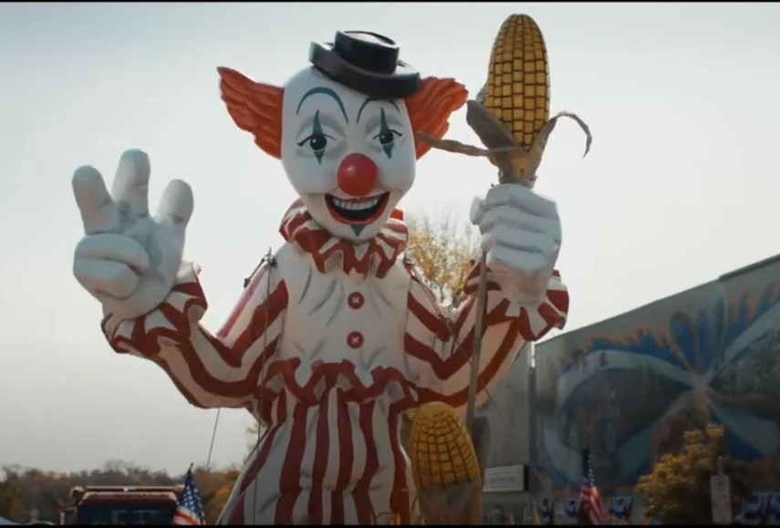 Clown in a Cornfield movie trailer scene showing clown mascot statue holding an ear of corn. Clown in a Cornfield movie trailer scene showing clown mascot statue holding an ear of corn.